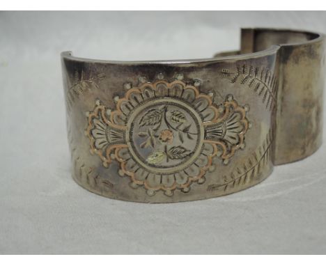 A Victorian silver hinged cuff bangle having engraved and yellow metal applique decorationHinge good, docoration good. Some w