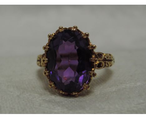 A lady's dress ring having a colour treated oval amethyst in a moulded collared mount to decorative shoulders on a 9ct gold l