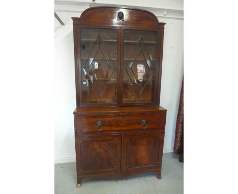 A Regency mahogany secretaire bookcase, arched cresting above a glazed rectangular doors flanked by reeded angles, the projec