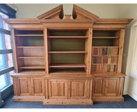 A 20th century pine breakfront bookcase in the manner of William Kent, the moulded broken architectural pediment over open sh