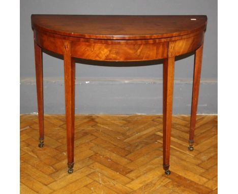 A George III mahogany card table, the demi lune foldover top over a plain frieze raised on inlaid square tapered legs and cas