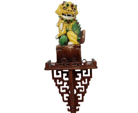 Chinese egg and spinach glaze foo dog sitting on a hardwood open work wall bracket. Measurements: 14 x 6 x 3 in.