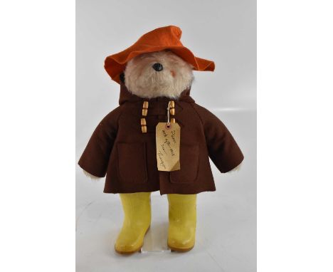 A vintage Paddington Bear with orange hat, brown coat and luggage tag inscribed 'Darkest Peru to London England via Paddingto