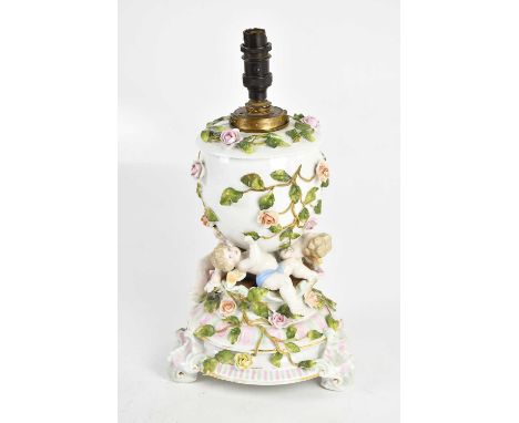 A late 19th century Continental porcelain oil lamp with floral encrusted decoration, the reservoir supported by three cherubs
