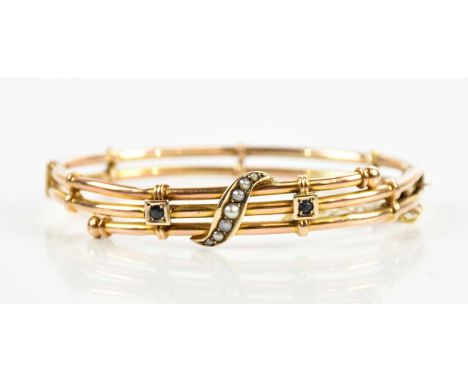 A 9ct yellow gold sapphire and seed pearl oval hinged bangle, set with a swept row of cut seed pearls and twin dark sapphires