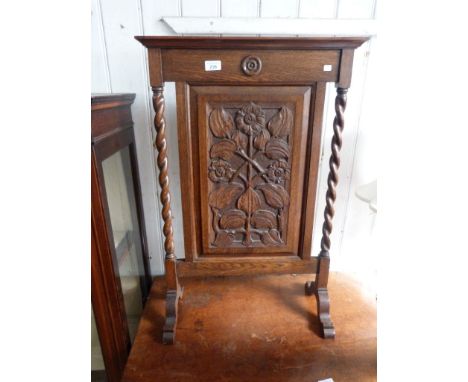 A 1920s carved oak fire screen, the central panel carved decoration of flowers, flanked by barley twist supports.