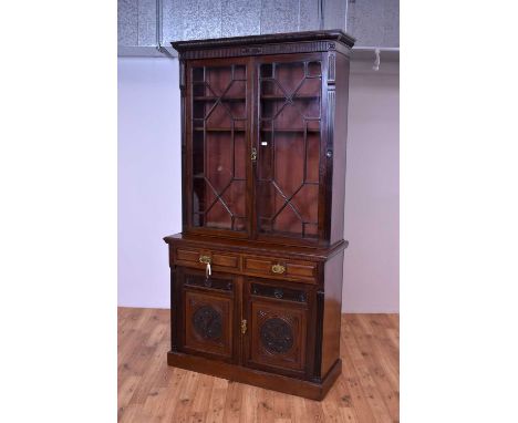 An early 20th Century mahogany carved and glazed bookcase, the flared top over a double door astragal glazed cabinet, atop tw