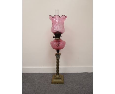 A Victorian cranberry glass oil lamp with frilled floral shade over etched glass reservoir above a brass twist column with en