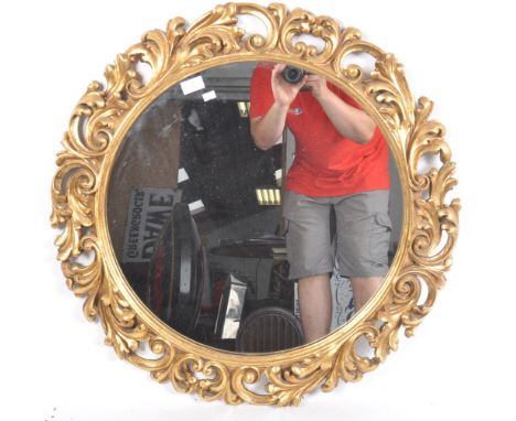 A vintage 20th Century Italian Hollywood regency gilt framed mirror having a circular mirror plate with pierced foliate and l