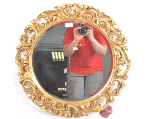 A vintage 20th Century Italian Hollywood regency gilt framed mirror having a circular mirror plate with pierced foliate and l