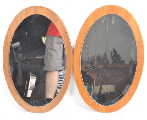 A matching pair of retro mid 20th Century teak framed hanging mirrors of oval form housing a single mirrored panel. Hanging h