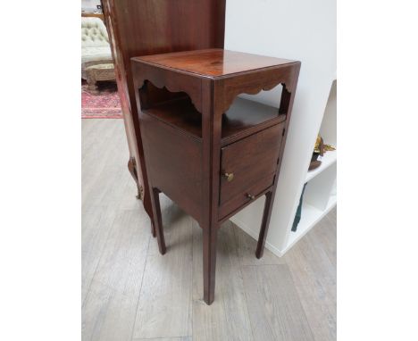 A George III mahogany nightstand, the wavy frieze and shelf over a single door cupboard and base drawer on chamfered square l
