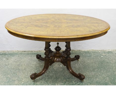 An oval burr walnut centre table, the four column base with volute feet and stiff leaf terminals, vase finial to stretcher, 1