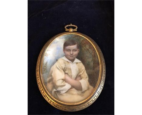 An Oval Miniature showing a Young Boy sitting with folded arms in front of a wooded background, carved and gilded bronze fram