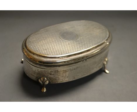 A George V silver oval trinket box, engine turned hinged cover, central circular vacant cartouche, silk lined interior, resti