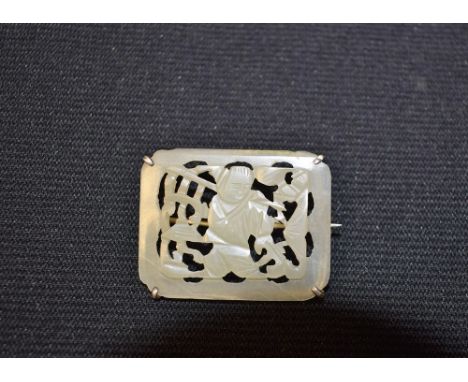 A rounded rectangular jade open work brooch, the centre carved and pierced with an oriental figure in landscape, silver colou