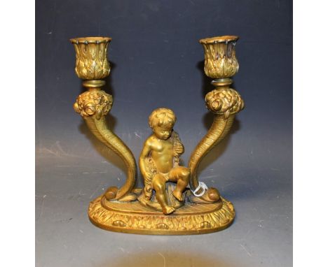 A gilt metal table candlestick, cast with a single central putto, flanked by a pair of corn-u-copia supports, late 19th centu