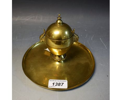 A Victorian brass desk inkwell, hinged cover with knop finial, parakeet masks to sides, crenellated socle, broad dished circu