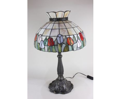 A Tiffany style table lamp, the leaded glass shade with tulip design, on bronzed base modelled as leaves and flowers, 64cm hi