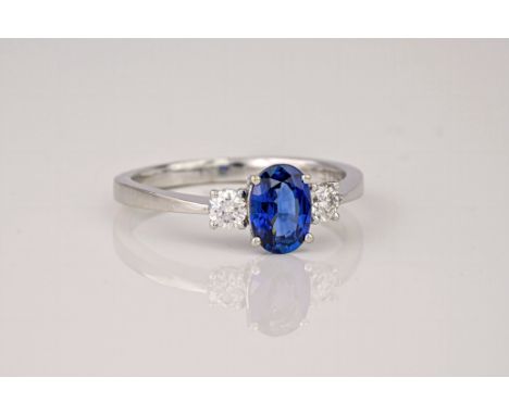 A white gold, sapphire and diamond three stone ring, the central oval cut sapphire of a deep, royal blue colour and flanked b