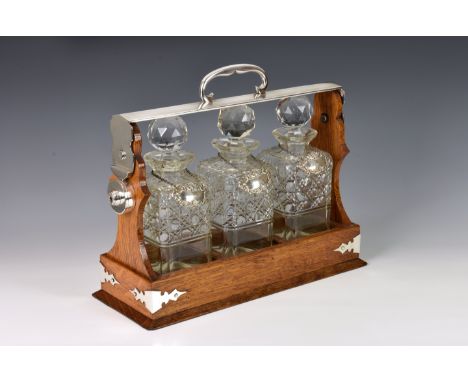 An oak three decanter Tantalus, late 19th / early 20th century, with silver plated fittings, the three decanters with diamond