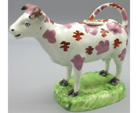 Early C19th Cambrian Pottery cow creamer, the pink lustre and red enamel spotted animal standing on an oval green naturalisti