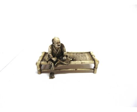 A JAPANESE IVORY OKIMONO  carved as a man sat on a low table, with inset red lacquer character mark to base, 9cm long.