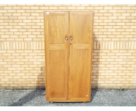 An Ercol twin door wardrobe measuring approximately 183 cm x 91 cm x 55 cm, supported on large castors and with original key.