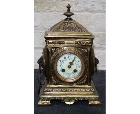 A late 19th century French brass mantle clock, the heavily cast architectural form case with mask ring handles and a painted 
