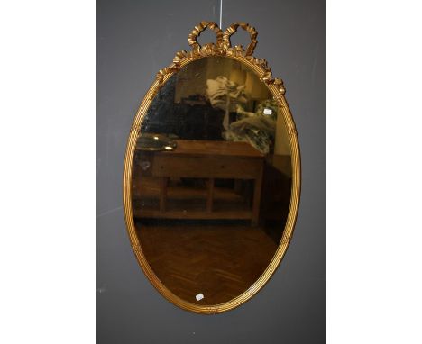 A Regency giltwood and gesso wall mirror with ribbon tied reeded oval frame and plain plate. 102 x 63 cms.