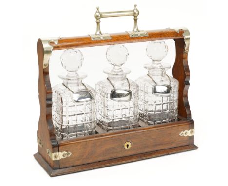Edwardian oak three bottle tantalus with cut glass decanters, each with silver plated labels, metal bound case with lockable 