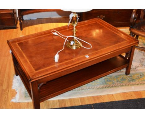 A modern mahogany two tier coffee table, raised on plain supports, 107cm long, together with a brass effect table lamp, with 