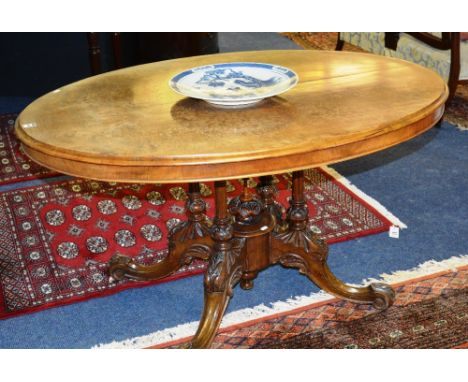 A Victorian walnut loo table, the moulded oval quarter veneered top, raised on fluted group columns, acanthus carved down swe