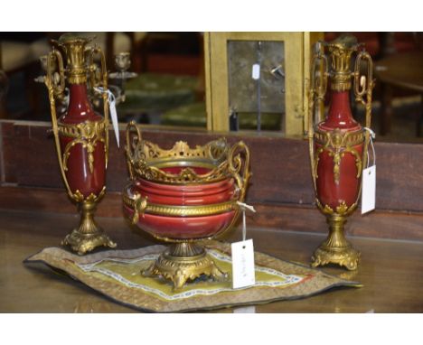 A three piece garniture set, each with red ceramic bowl, pierced floral gilt metal collar, scroll handles and fluted plinth b