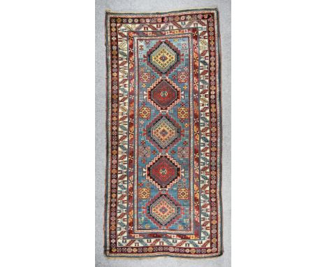 An Early 20th Century Kazakh Runner woven in colours of ivory, navy blue and wine, with five bold central stepped lozenge-sha