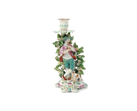A Derby candlestick figure of a piping shepherd  c.1765, standing before flowering bocage rising to a candle sconce, his dog 