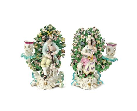 A pair of Derby candlestick figures of musical shepherds  c.1765-70, each seated before elaborate flowering bocage, he playin