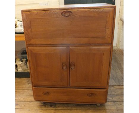 A mid Century Ercol elm cabinet, with fall front enclosing two small shelves, above a pair of cupboard doors enclosing a furt