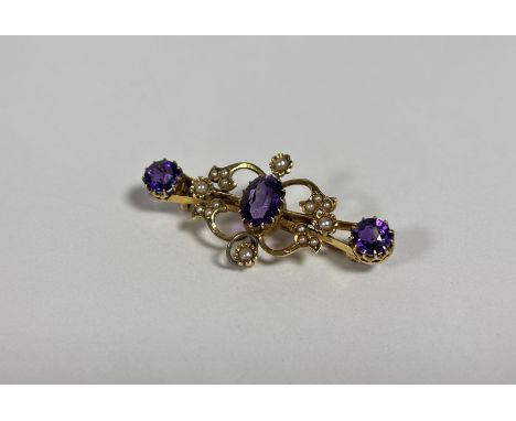 An Edwardian 15ct gold, amethyst and seed pearl brooch, centred by an oval-cut amethyst, the split bar of foliate form and se