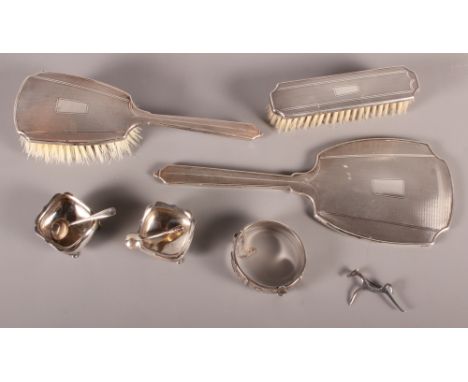 A silver backed three-piece dressing table set, a pair of silver salts and spoons, a silver brooch and a silver hinged bangle