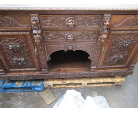Late Victorian oak side board with two drawers enclosed by a pair of doors, carved with scrolls, lion and cherub mask heads a