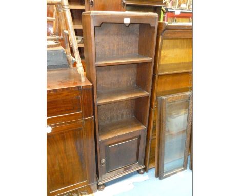 A 1940's Oak narrow two shelf Open Bookcase on lower single raised and folded panel door with iron handle, standing on turned