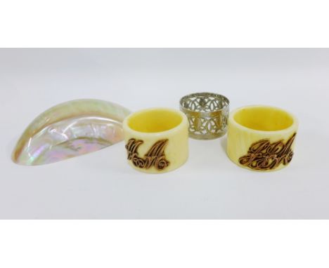 Two early 20th century ivory napkin rings, each with a yellow metal monogram together with a silver plated napkin ring and an