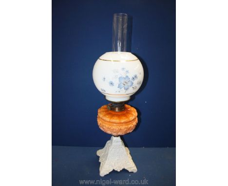 An Oil Lamp with orange opaque glass reservoir and white shade with blue flowers on cast base.