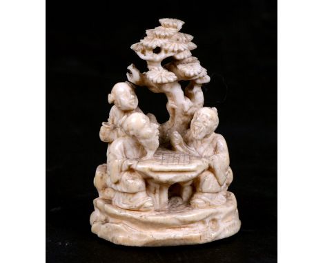 A 19th century Chinese carved ivory group depicting old men playing board games under a tree, 6.25cms (2.5ins) high.