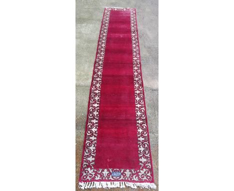 A Persian Tabriz woollen hand knotted runner with red ground within floral borders, signature to one end, 490 by 85cms (193 b