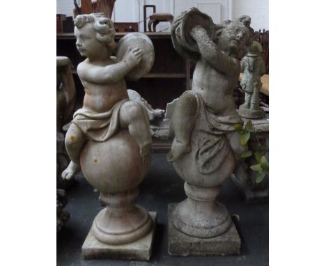 A pair of composite stone statues of cherubs playing tambourines and cymbals seated on globes (af) 105cmH