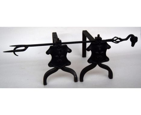 A pair of cast iron fire dogs with shield decoration together with a wrought iron fire fork with rams head detail