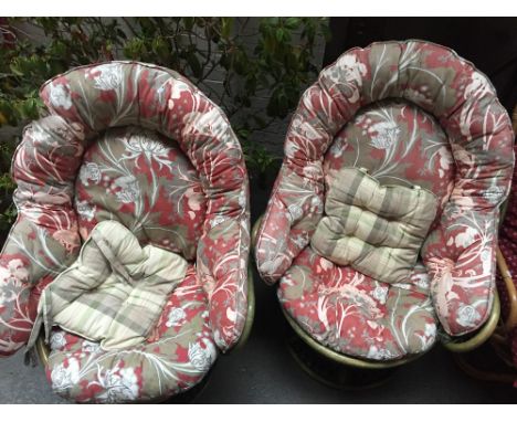 A pair of green rattan chairs with padded floral cushions together with another rattan chair with padded red cushion