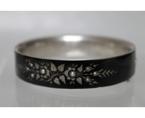 A VICTORIAN SILVER AND ENAMEL MOURNING BANGLE, with pique inlay and seed pearl embellishment, the inner edge with engraved de
